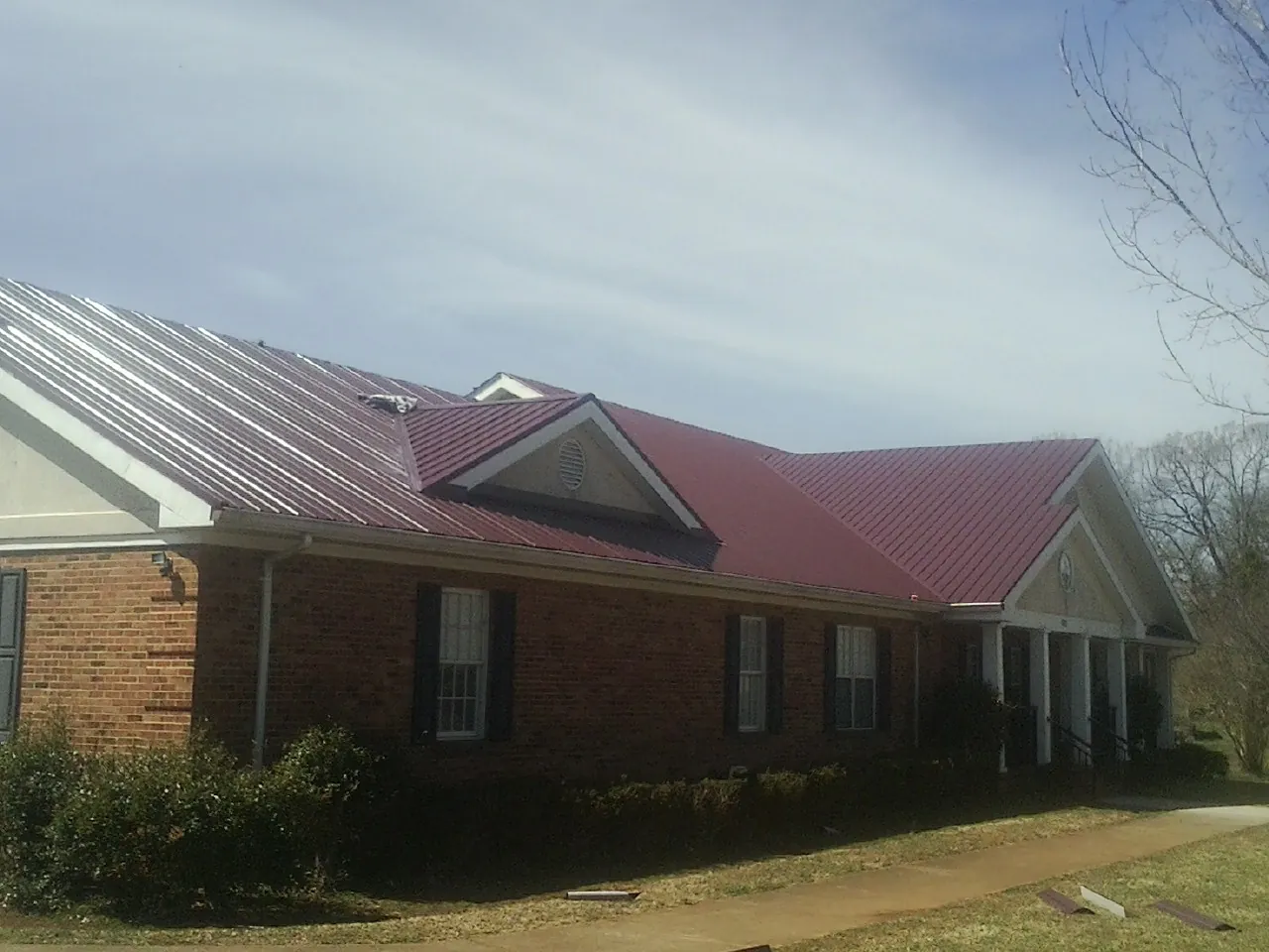 Red metal roof with gabled entries on a long brick building, from a Hail Damage Roof Repair job in Mountain Top