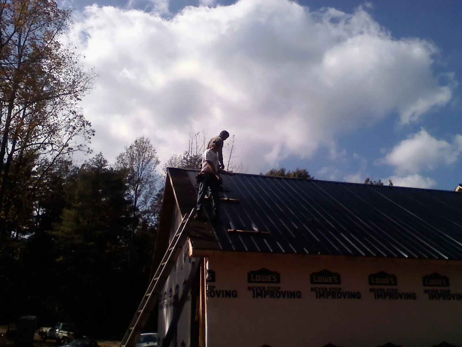 Roofer fastening dark metal panels high against a cloudy sky, from a Roof Inspection job in Mountain Top