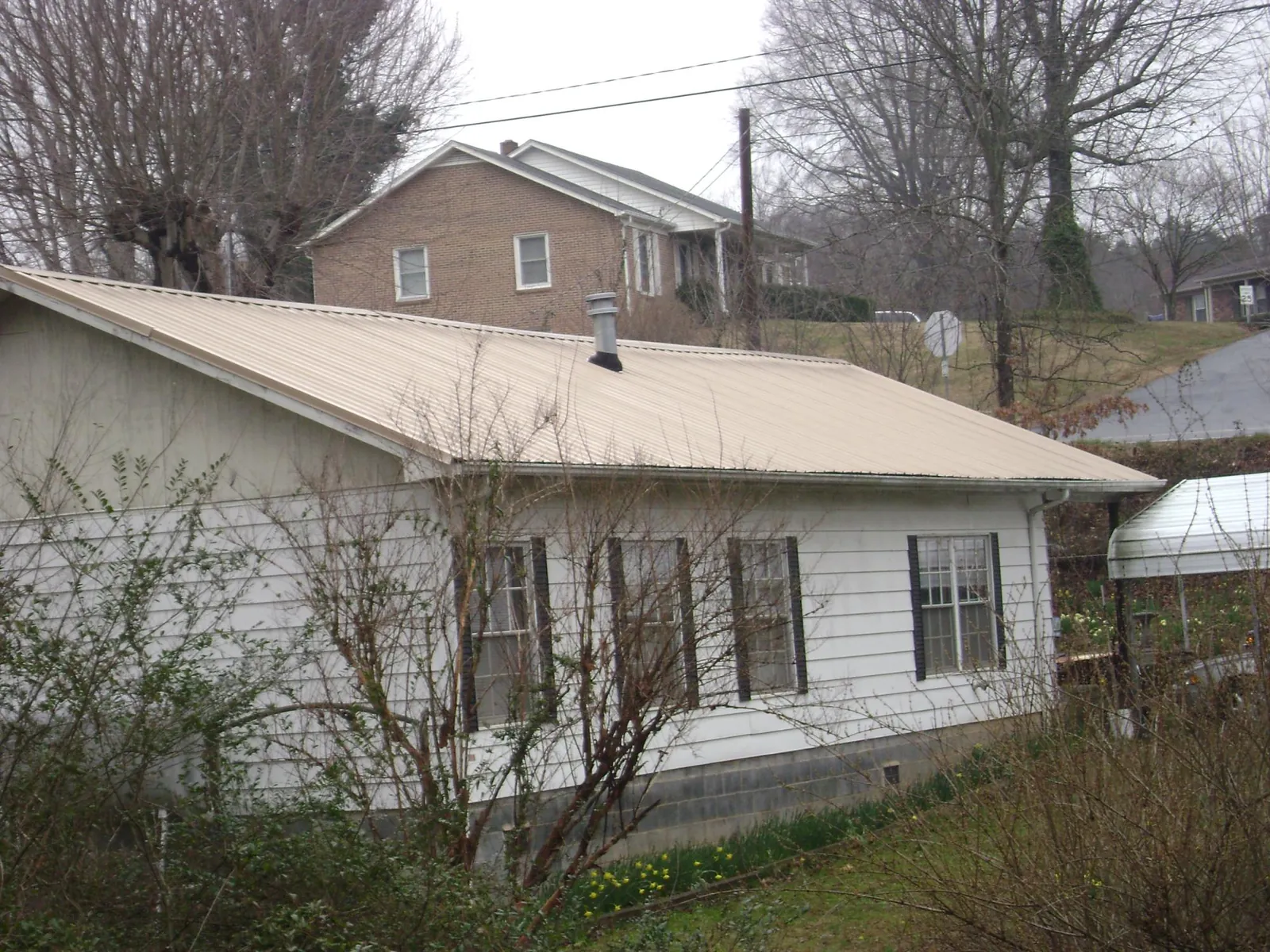 Tan metal roof on a white sided house set into a hillside — Commercial Roofing by Roofing Brothers in Mountain Top